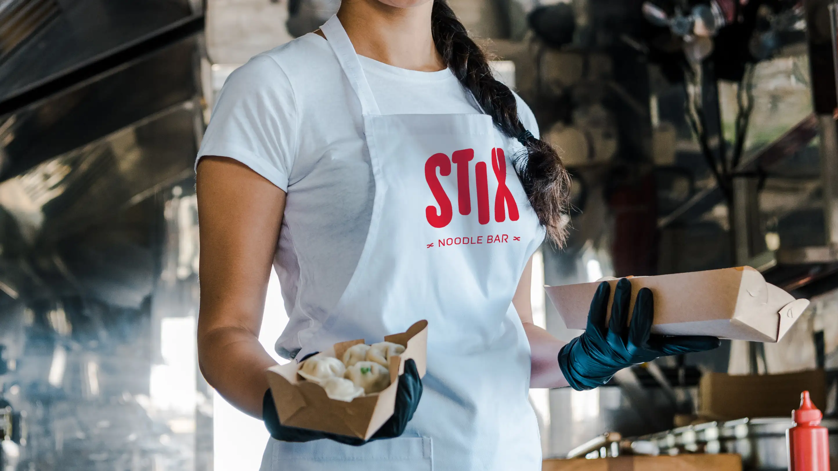 Food truck server wearing white apron featuring Stix Noodle Bar logo design in red.